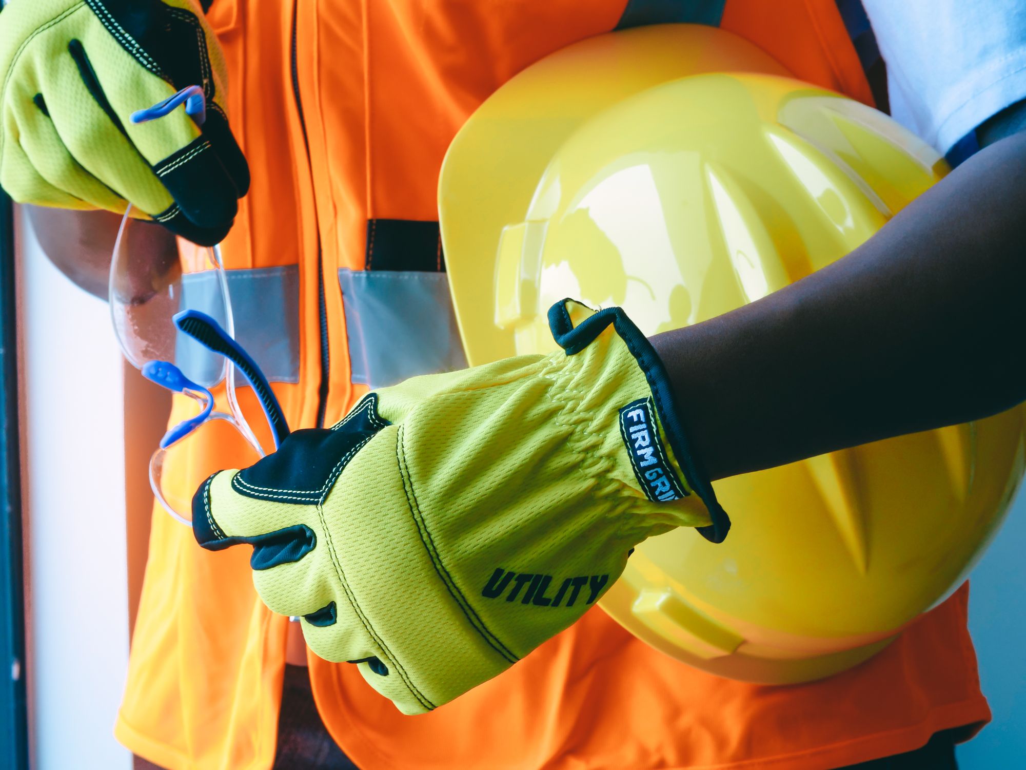 Worker in hi-vis vest holding a safety helmet, gloves and safety glasses